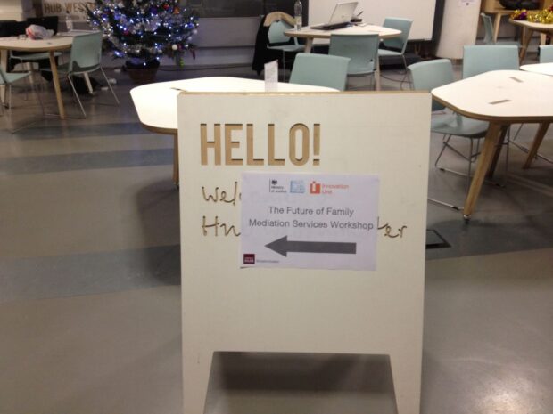 A sandwich board is set up on the floor with a paper sign on it saying 'hello' and pointing people into the workshop room.