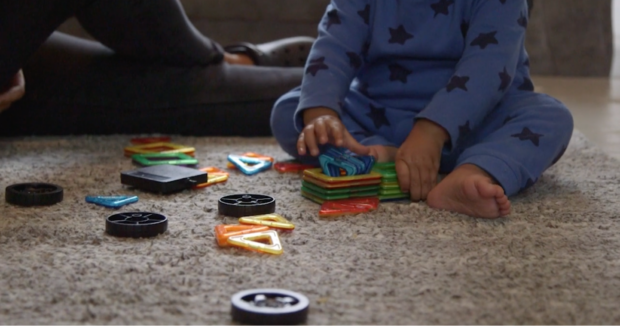 Photo of a young child sitting carpeted floor playing with toys, taken from the eye level of the child. Child's face isn't shown.